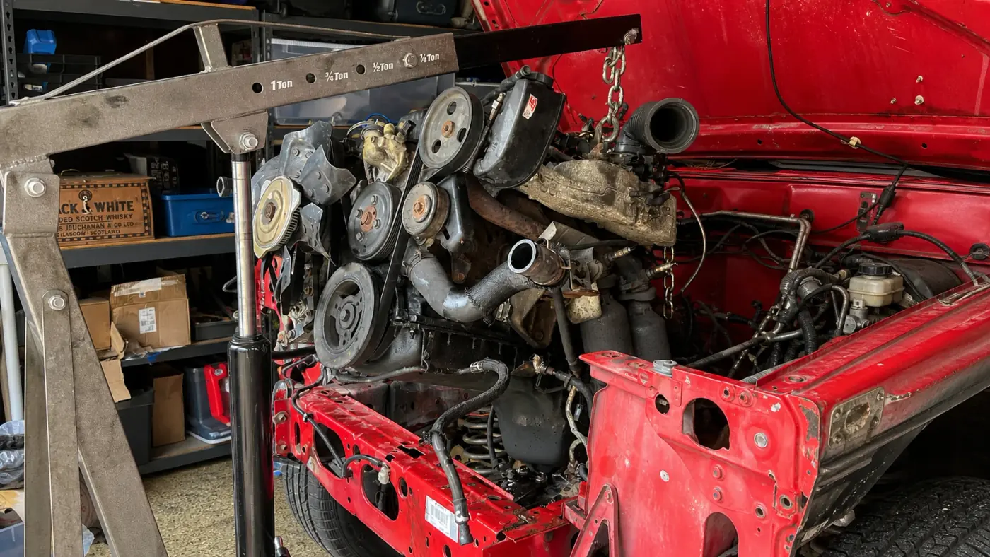 Engine hanging from a shop crane above an open engine bay