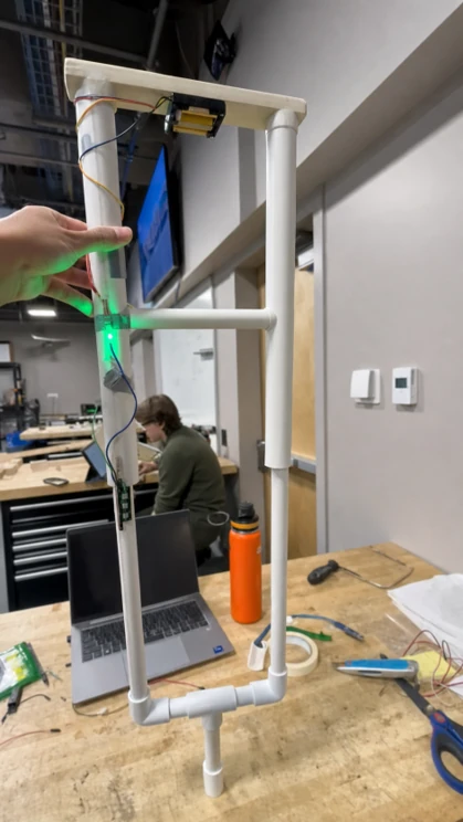 Telescoping crutch prototype built from white PVC pipe, held upright in a lab, with a green indicator light lit