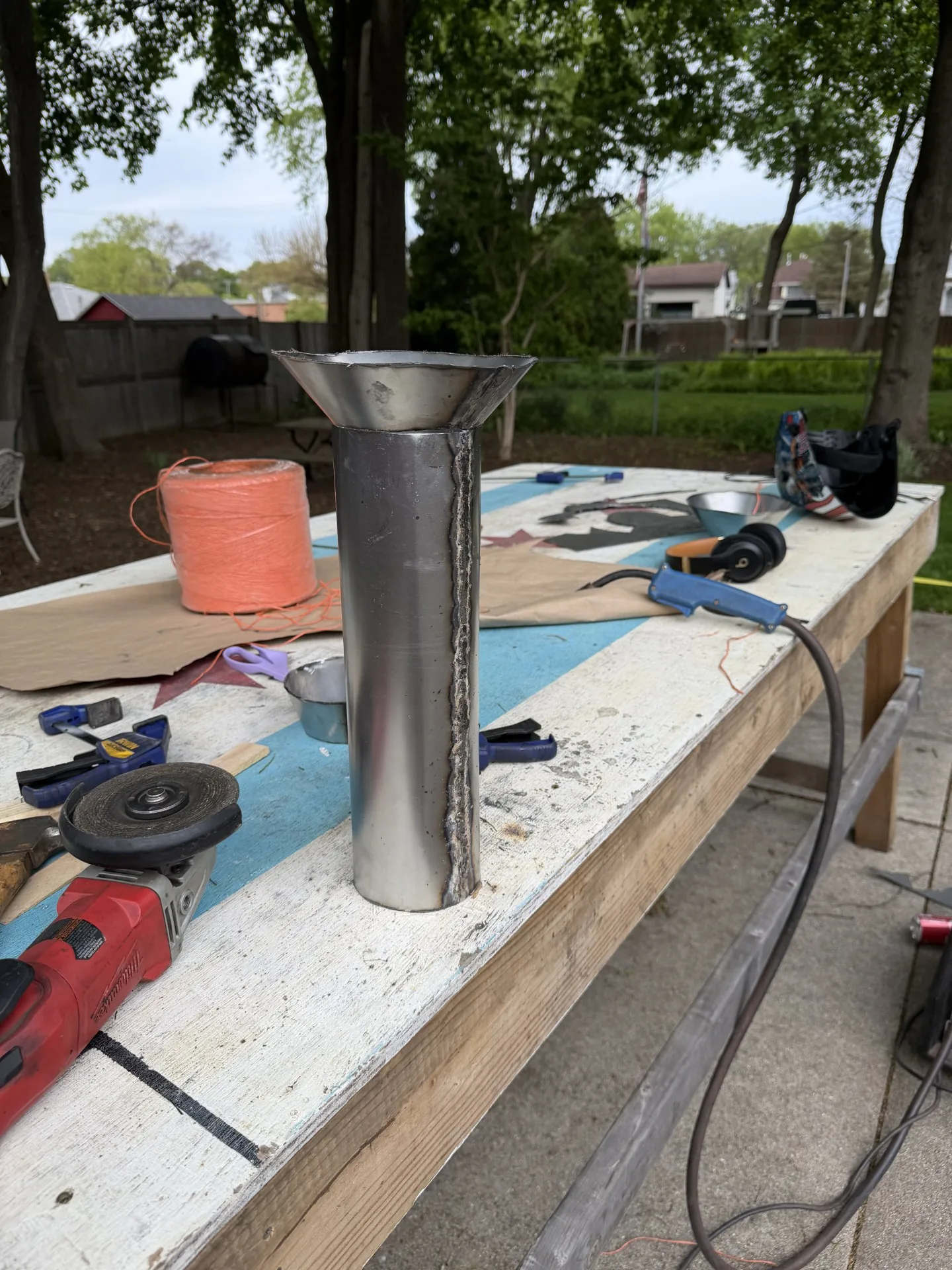 Fabricated steel pulse jet standing upright on an outdoor work table next to an angle grinder