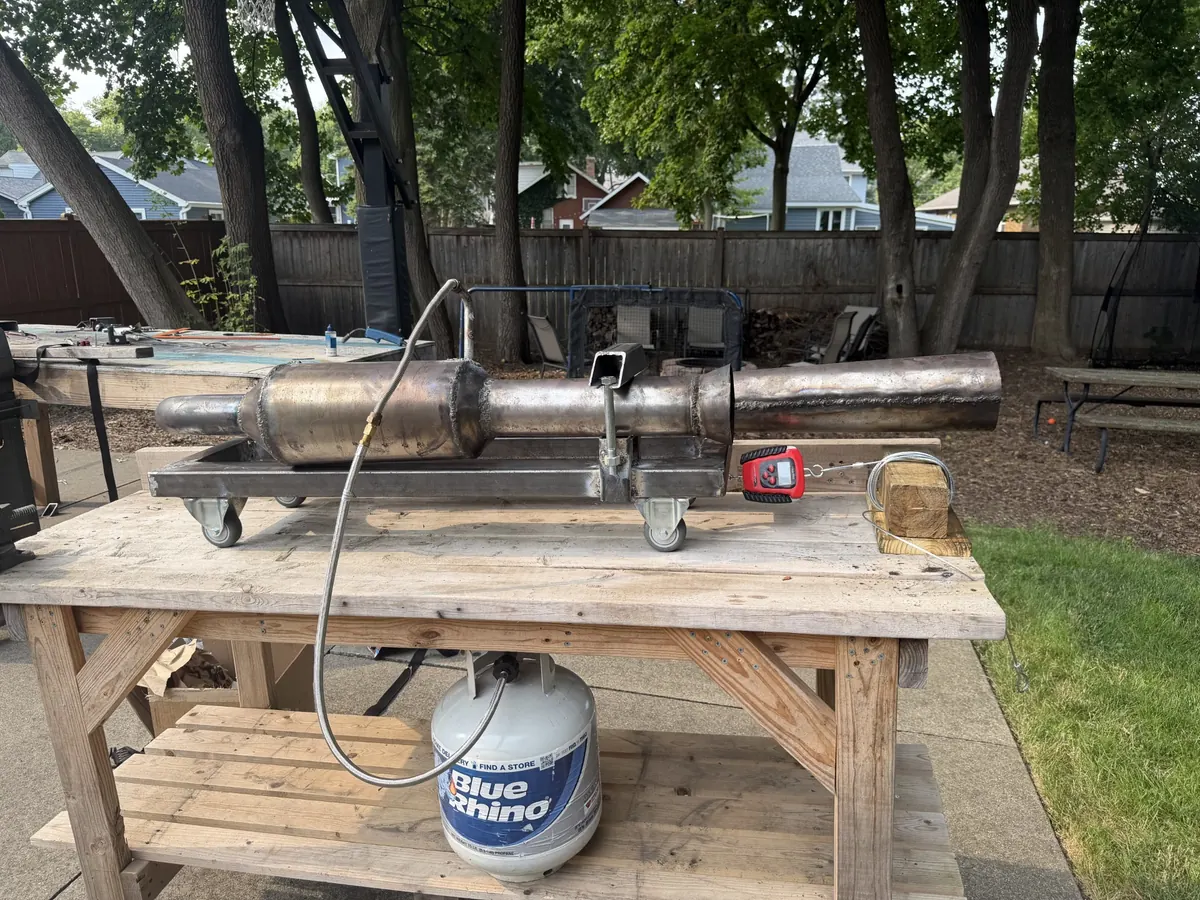 Steel pulse jet mounted on a wheeled frame on a wooden work table, fed by a propane tank on the shelf below